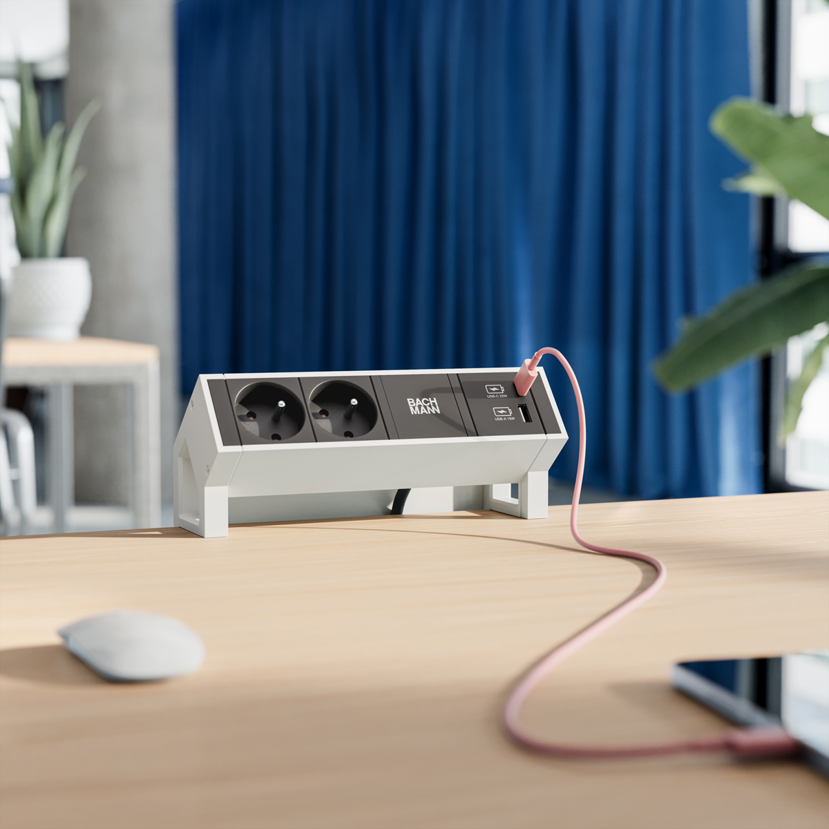 A white power strip with two outlets and USB ports stands on a wooden desk in front of blue curtains.