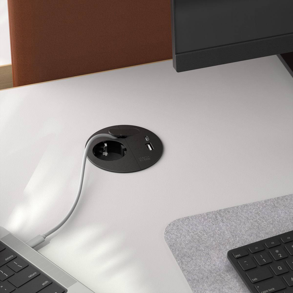 Ein weißer Schreibtisch mit integrierter schwarzer Steckdose, eingestecktem weißem Kabel, Tastatur und Monitor.