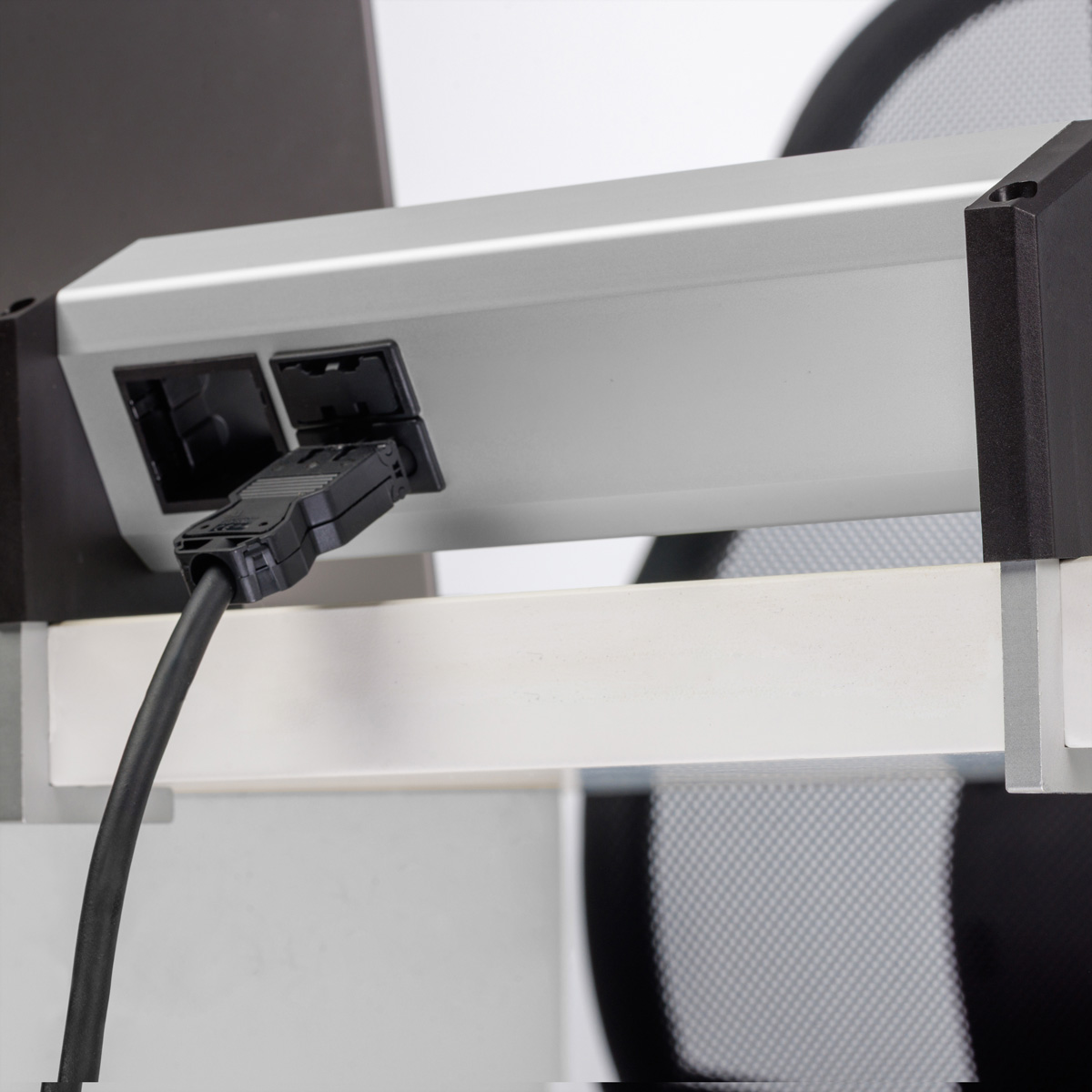 Ein schwarzes Kabel ist in eine silberne Steckdosenleiste am Schreibtisch eingesteckt.