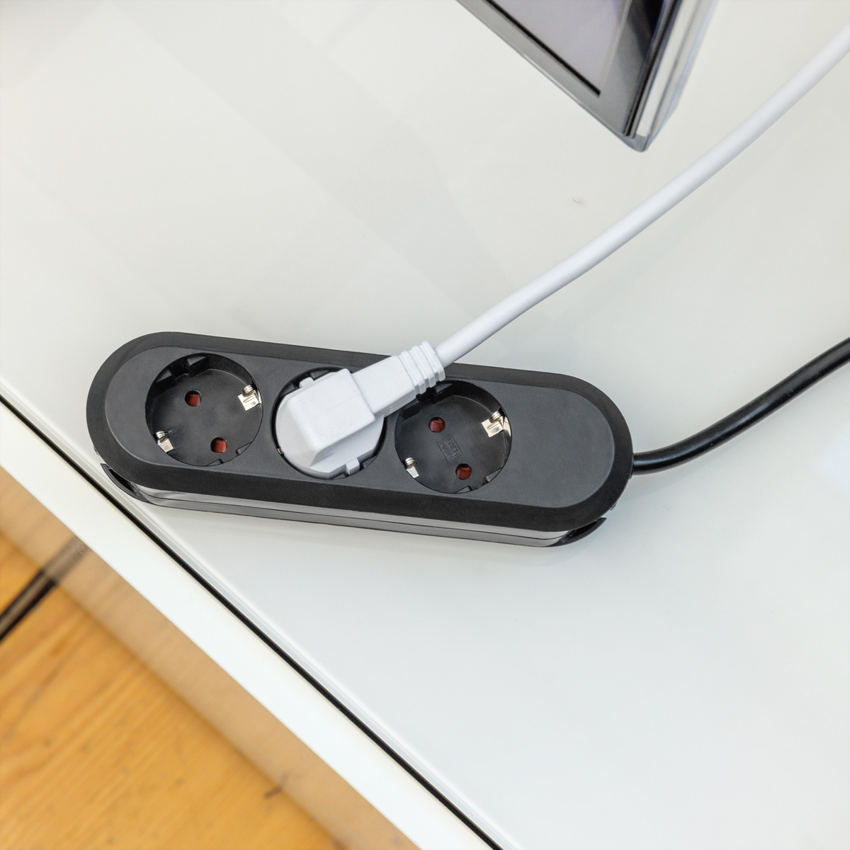 Eine schwarze Mehrfachsteckdose mit einem eingesteckten weißen Stecker liegt auf einer hellen Oberfläche.