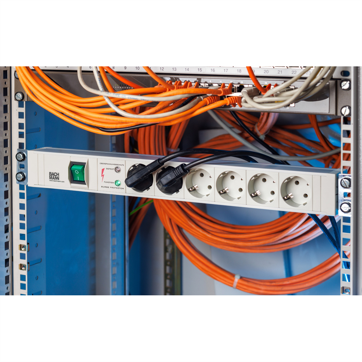 Eine weiße Steckdosenleiste mit zwei eingesteckten Kabeln in einem Netzwerkschrank mit vielen orangefarbenen Kabeln.