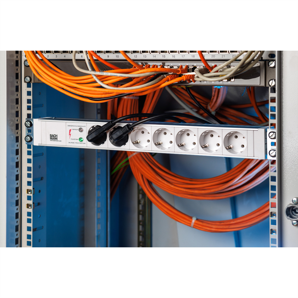 Una ciabatta bianca con due cavi neri collegati all'interno di un rack di server pieno di cavi arancioni.