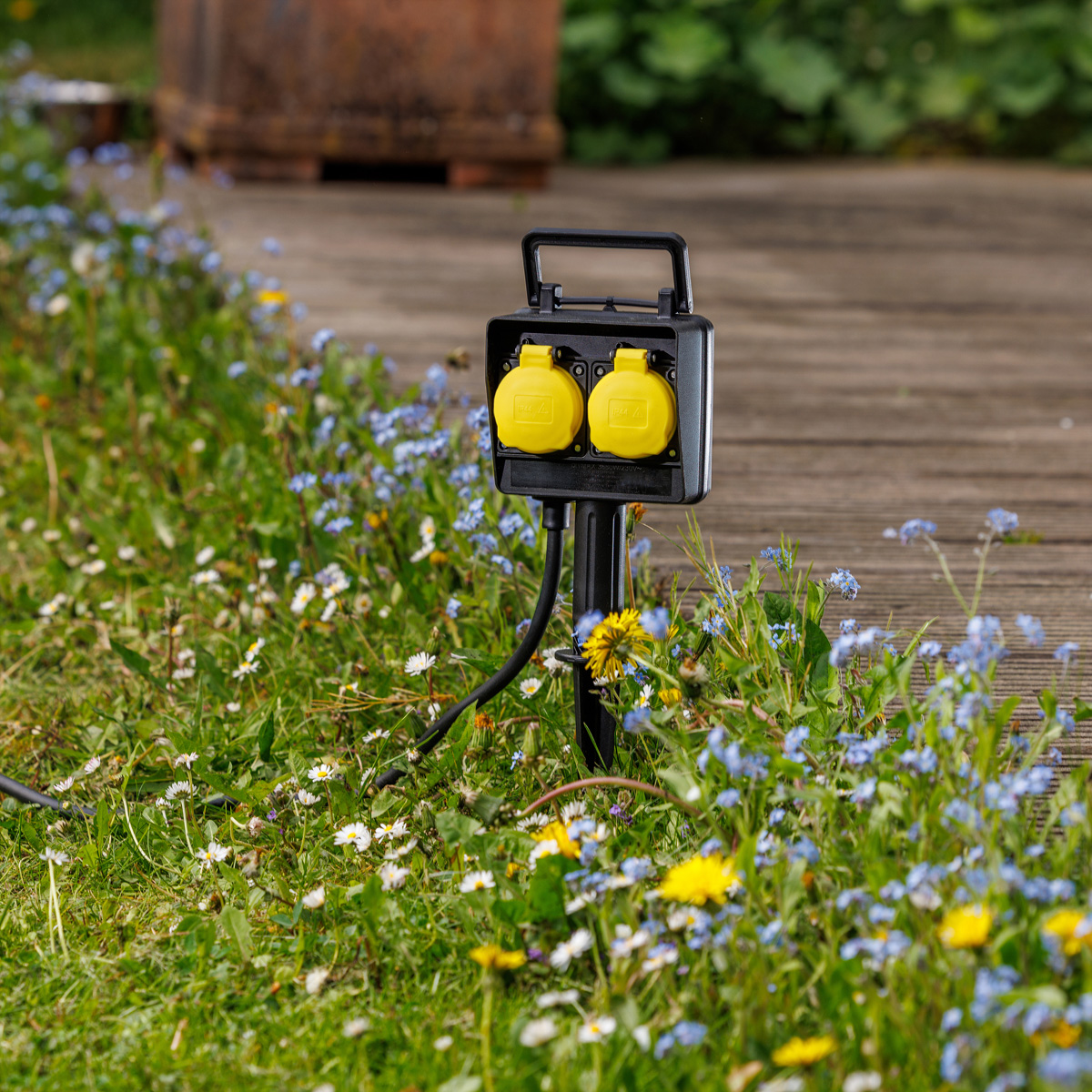 Eine schwarze Gartensteckdose mit zwei gelben Steckdosen in blühendem Gras.
