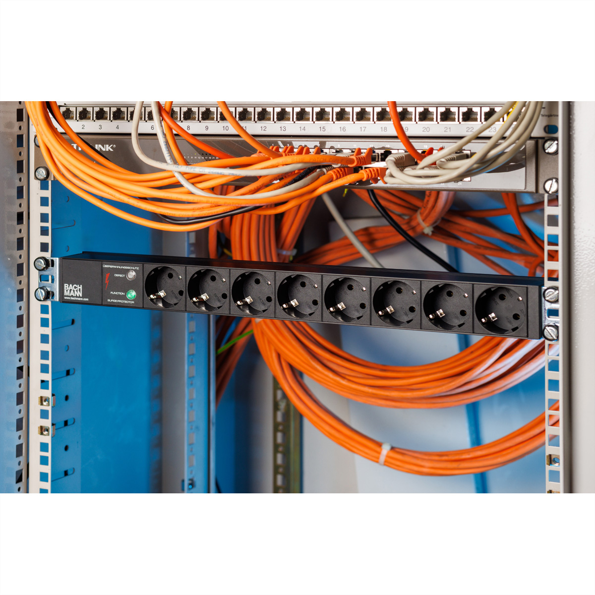 Eine schwarze Steckdosenleiste in einem Serverschrank mit vielen orangefarbenen Kabeln.