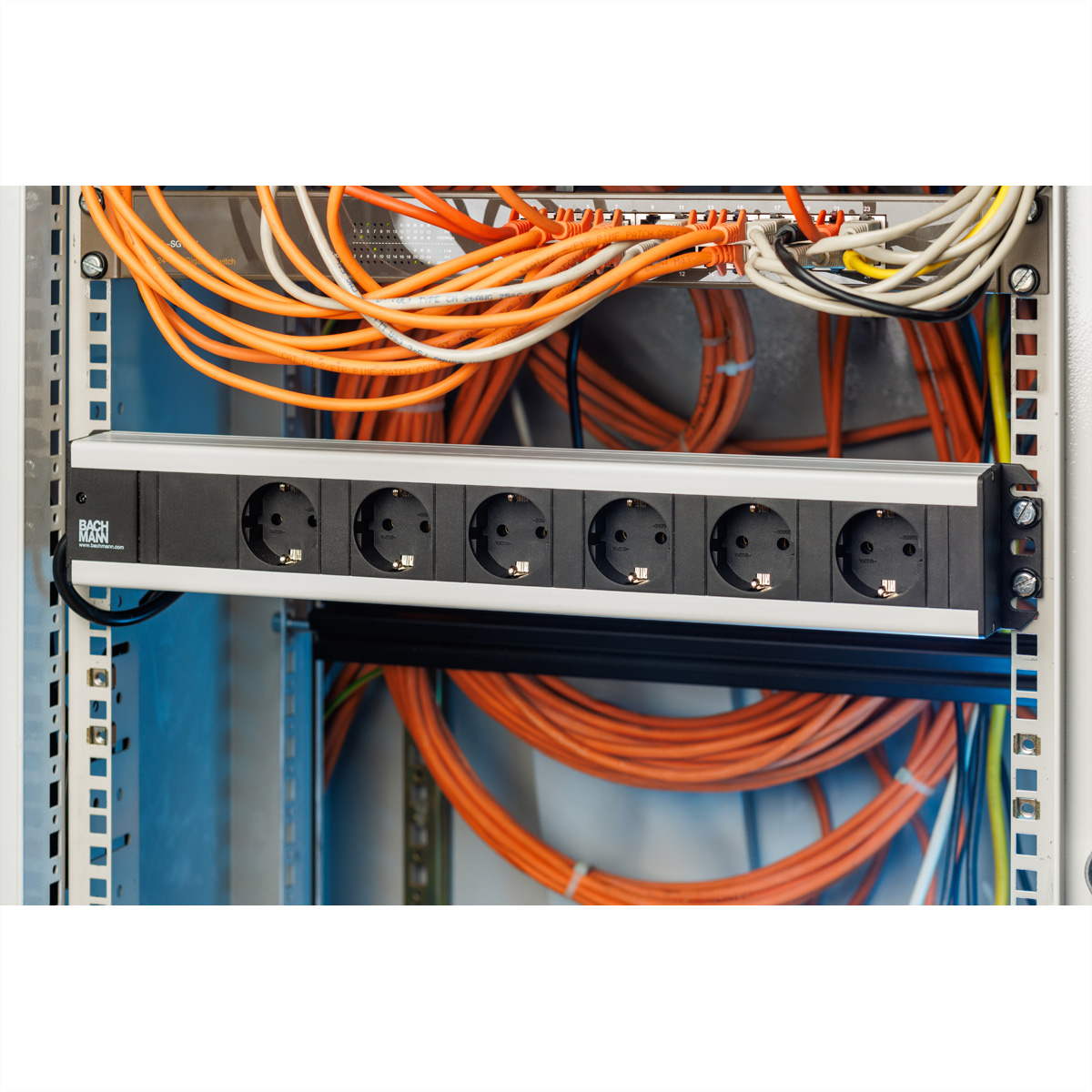 Ein Serverschrank mit einer schwarz-silbernen Steckdosenleiste, umgeben von orangefarbenen und weißen Kabeln.