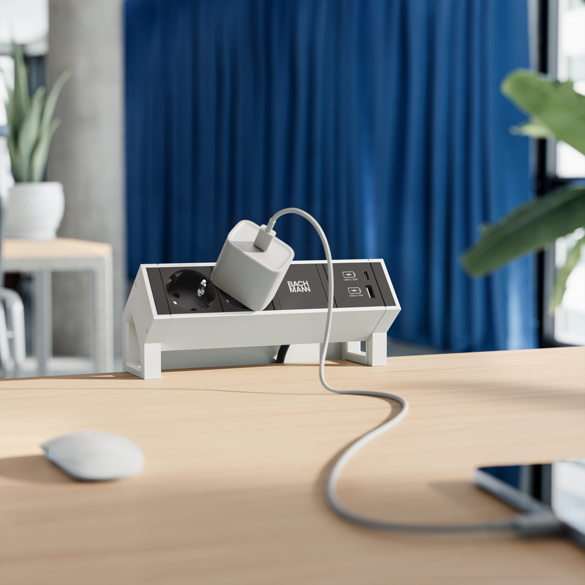 Une multiprise blanche Bachmann sur un bureau en bois avec un chargeur branché et un fond bleu.