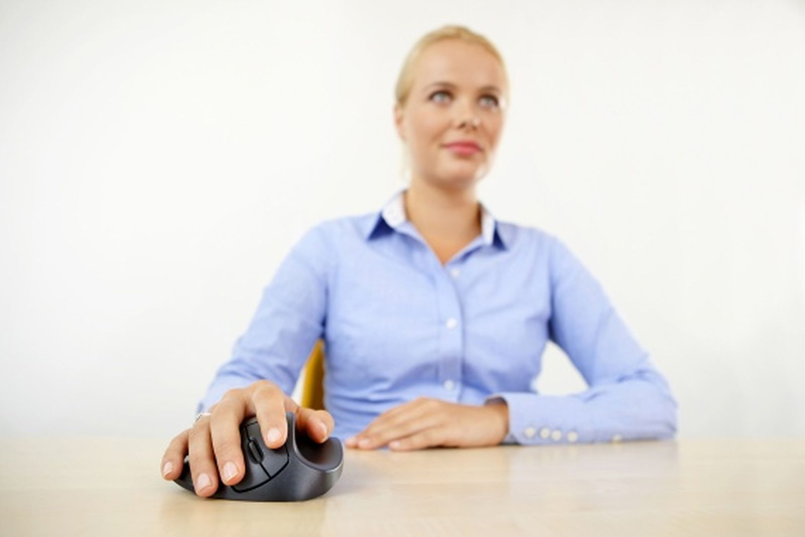 Una donna bionda con una camicia blu siede a una scrivania e usa un mouse.
