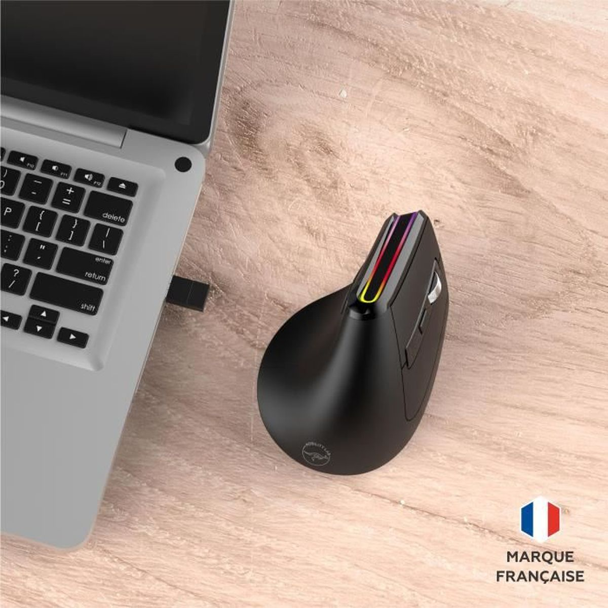 Un ratón vertical ergonómico negro con LED de colores está junto a una laptop en un escritorio de madera.