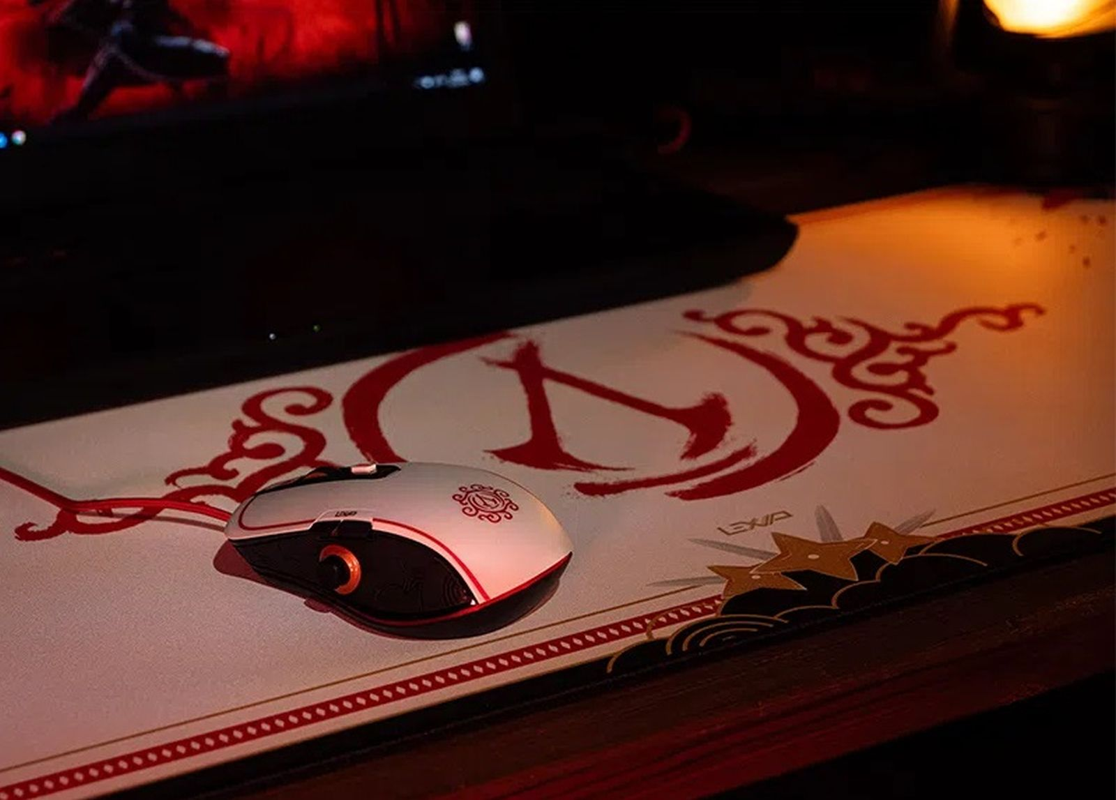 Un ratón de juego con cable blanco y rojo descansa sobre una alfombrilla roja a juego frente a un ordenador portátil.