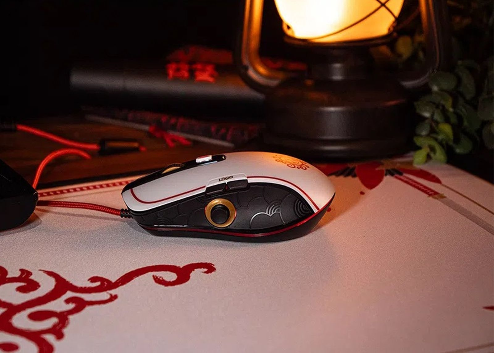 Un ratón de juego estilizado blanco y negro con detalles rojos descansa en un escritorio con una linterna.