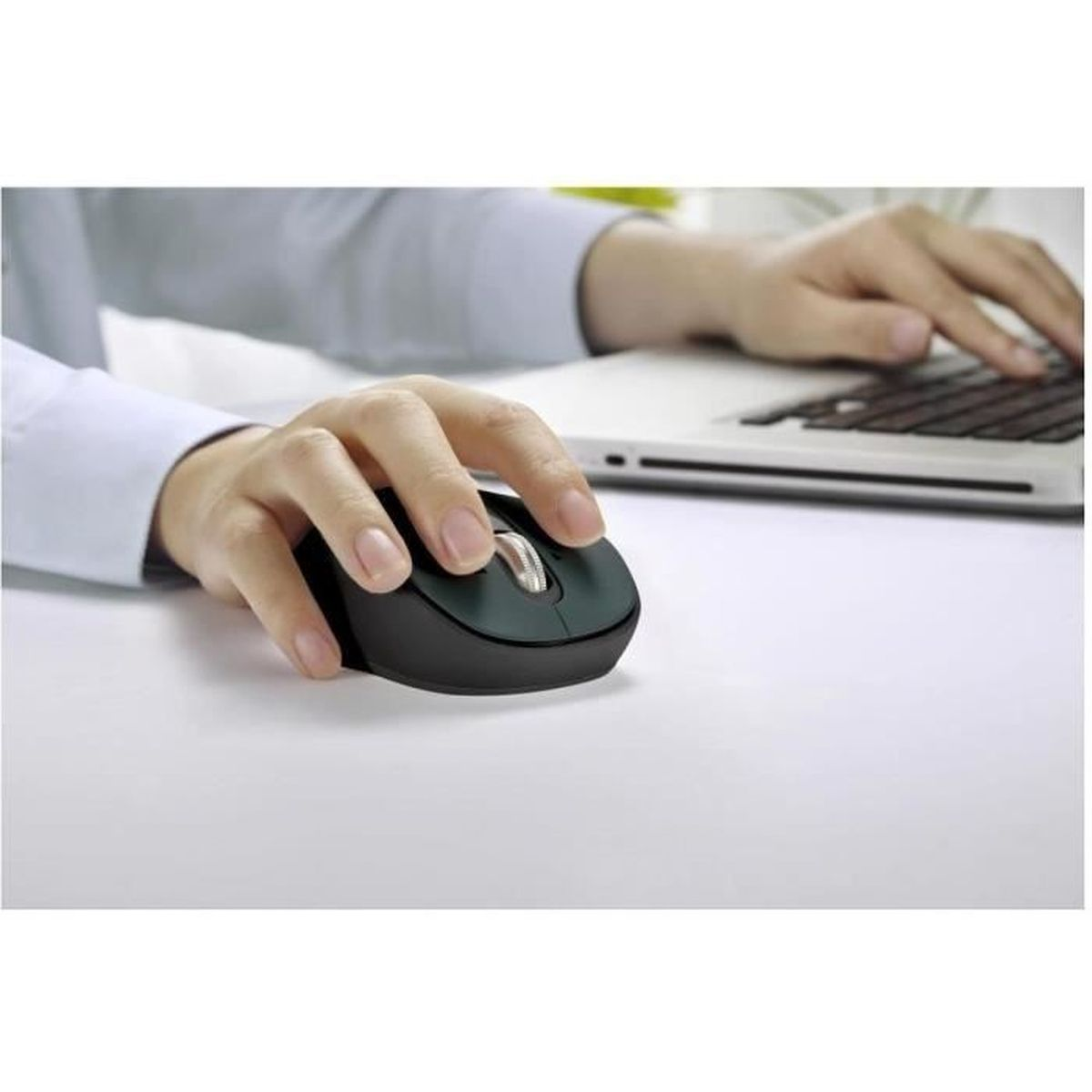 Una mano opera un ratón de ordenador negro en un escritorio blanco, con un portátil de fondo.