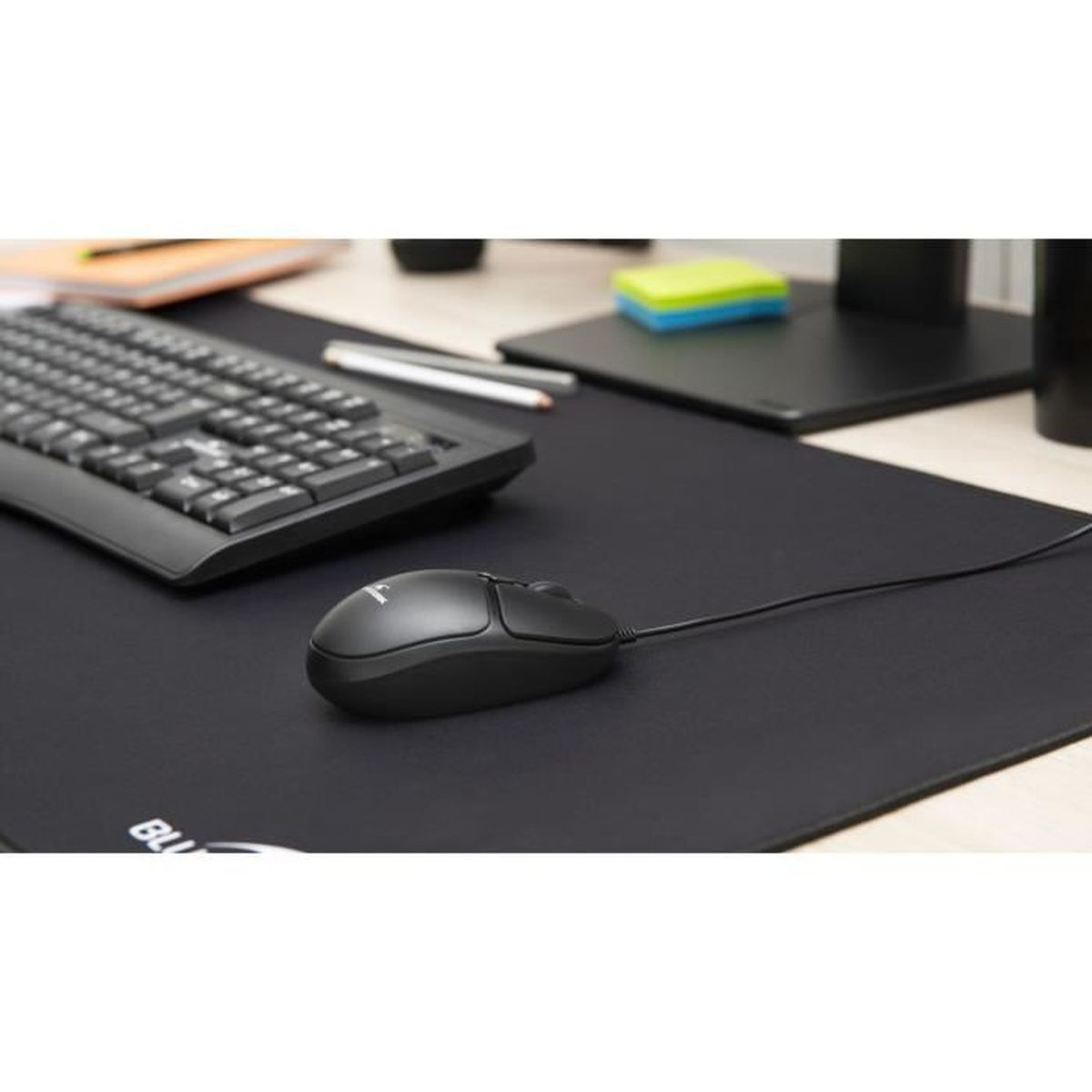 Un ratón de ordenador negro en una alfombrilla grande negra junto a un teclado en un escritorio.