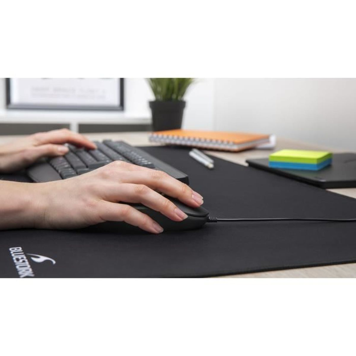 Un par de manos trabajan en un teclado y un ratón con cable en una esterilla de escritorio negra grande.