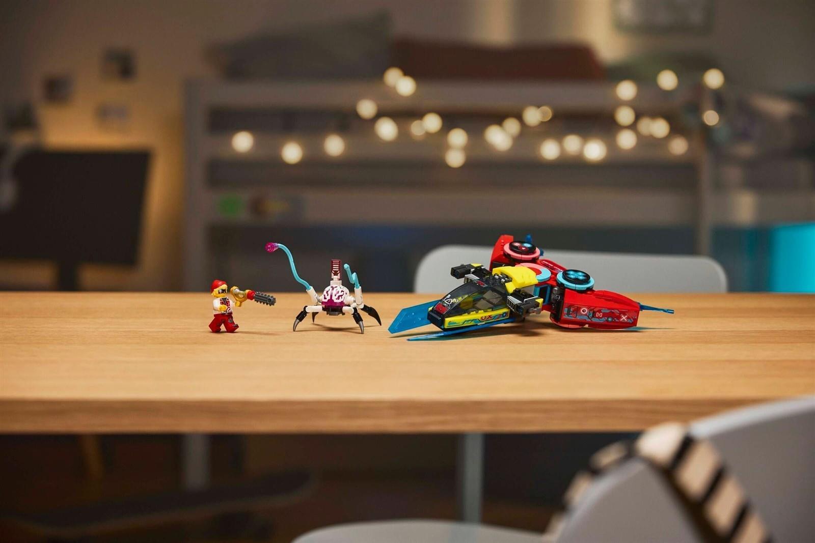 Lego-Minifigur, Spinnenroboter und rotes Raumschiff auf Holztisch in weich beleuchtetem Raum.