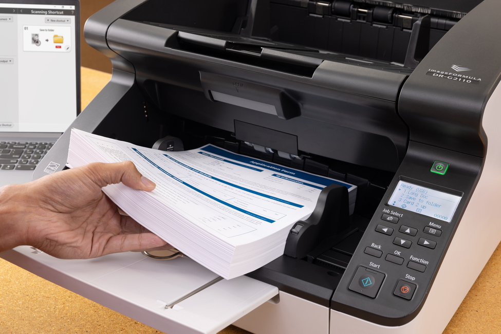 Eine Hand legt einen Stapel Anmeldeformulare in einen modernen Dokumentenscanner.