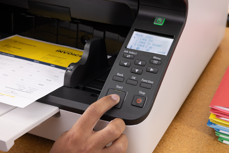 Eine Hand drückt den Startknopf an einem modernen Büroscanner, während eine Rechnung verarbeitet wird.