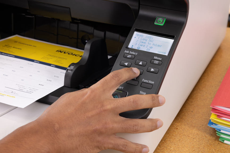Eine Hand bedient das Tastenfeld eines Scanners, während ein Dokument eingezogen wird.
