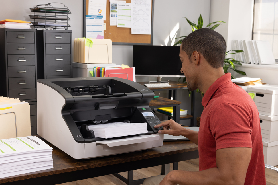 Ein Mann im roten Hemd bedient einen Dokumentenscanner in einem Büro.