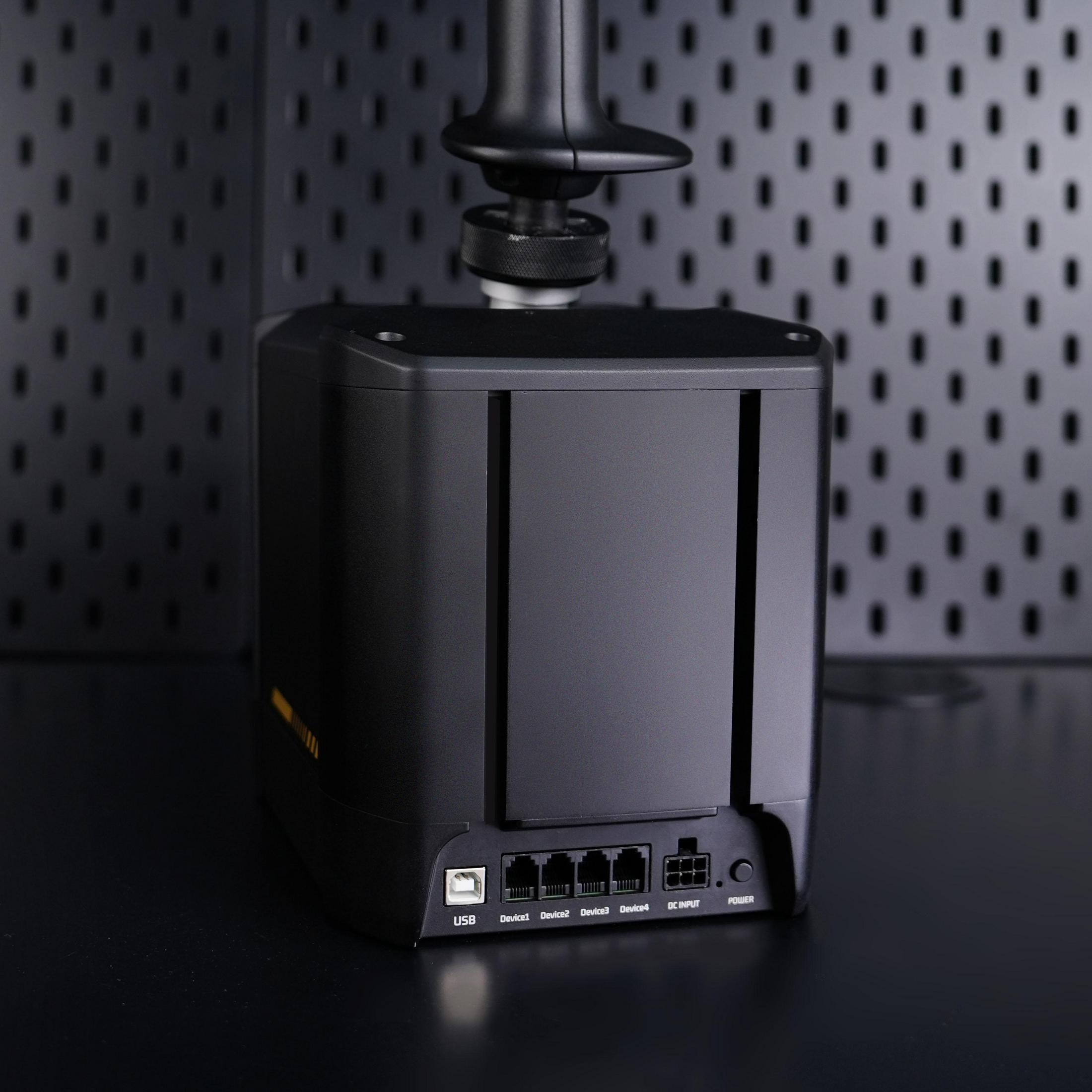 Schwarzes Steuergerät mit Anschlüssen und Joystick oben auf einem Tisch vor einer Lochwand.
