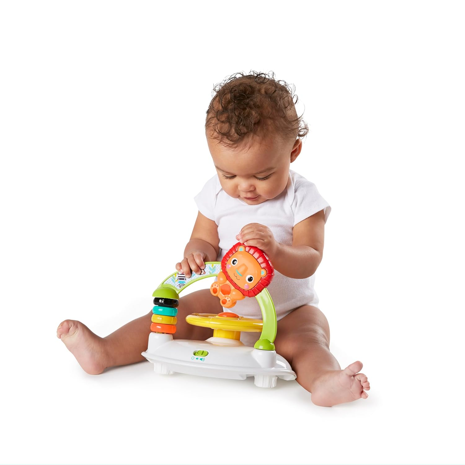 Un bambino in tutina bianca è seduto sul pavimento che gioca con un giocattolo educativo colorato.