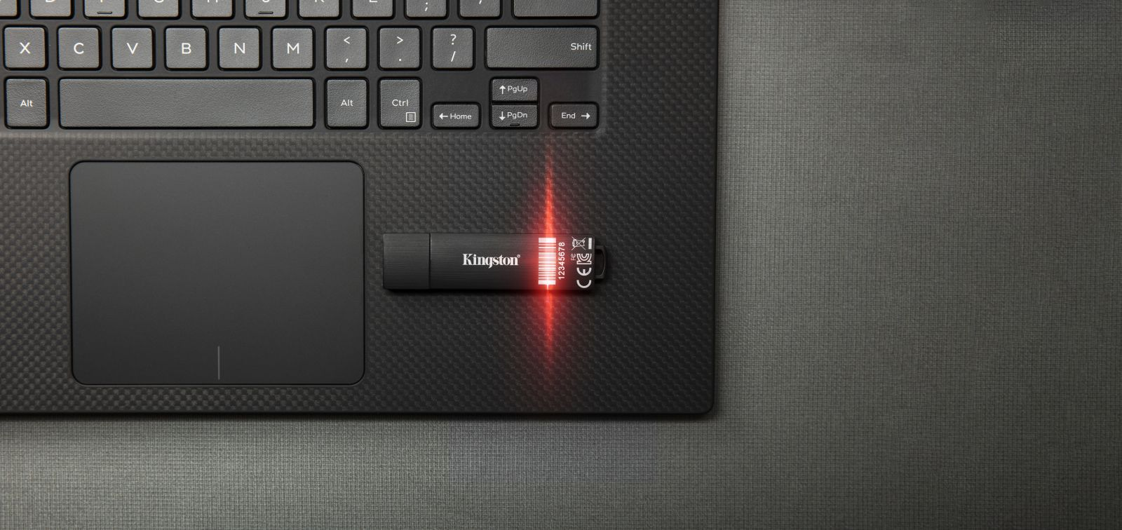 Una unidad flash USB Kingston negra conectada a una computadora portátil al lado del panel táctil, con una luz roja.
