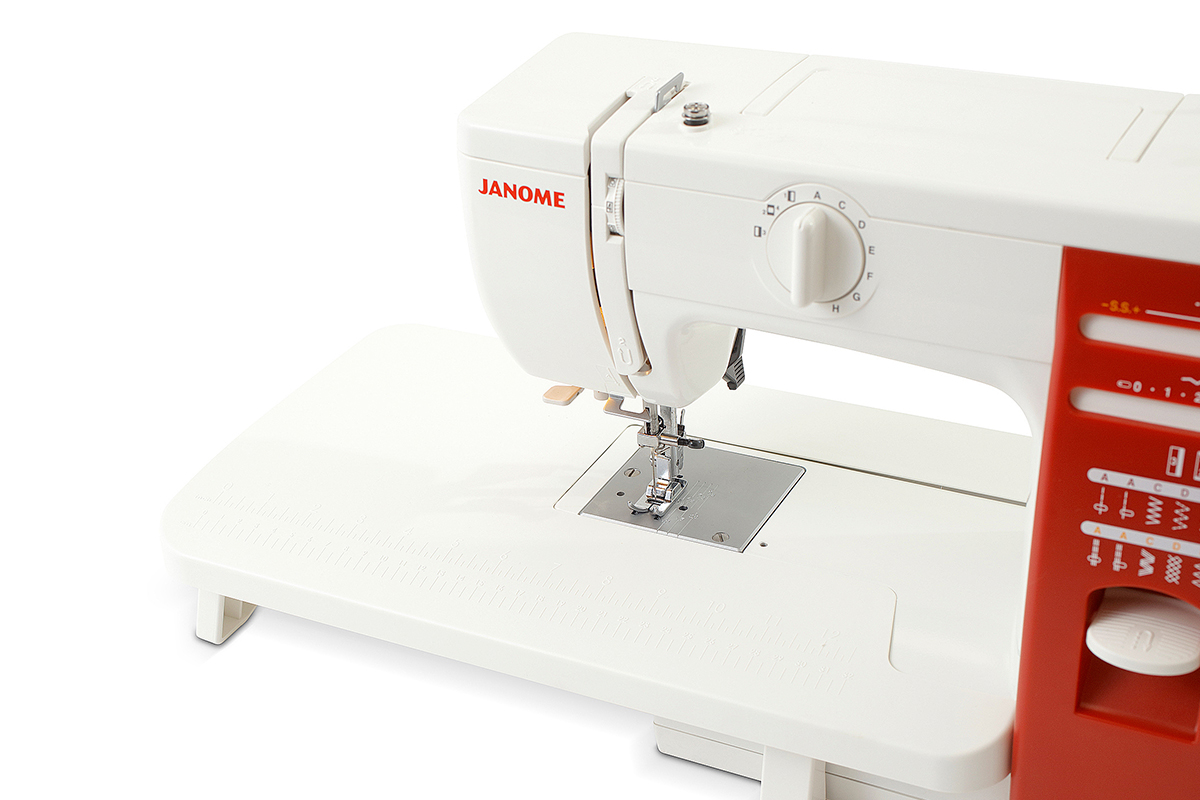 Una máquina de coser Janome blanca y roja con mesa de trabajo amplia sobre fondo blanco.