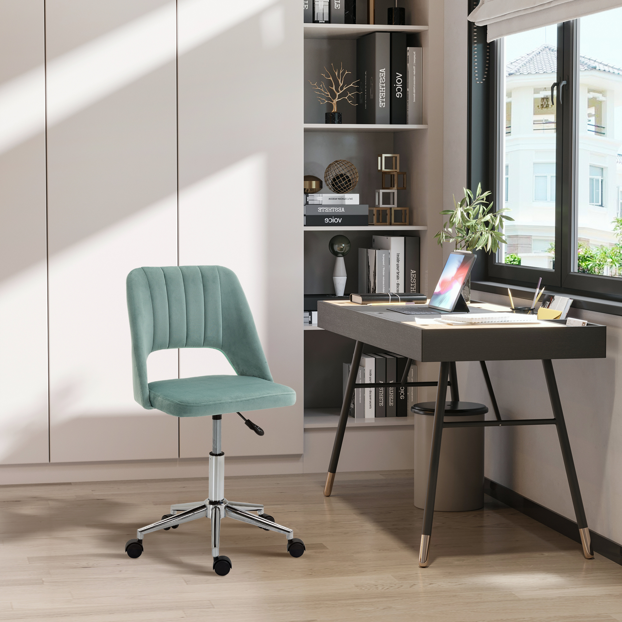 Una sedia da ufficio in velluto verde menta davanti a una scrivania scura con laptop e libreria.