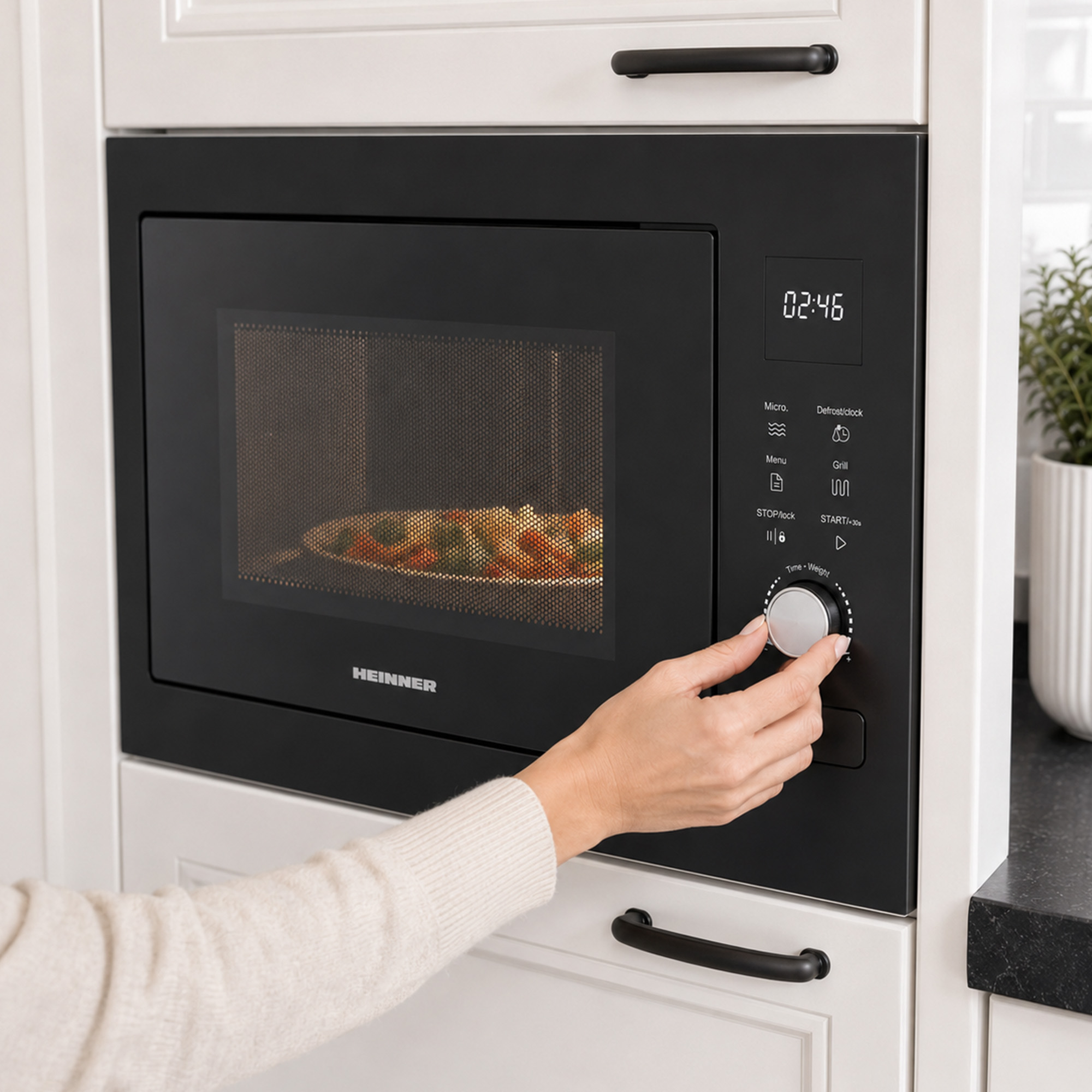 A hand turns the dial on a black built-in microwave, heating food visible inside.