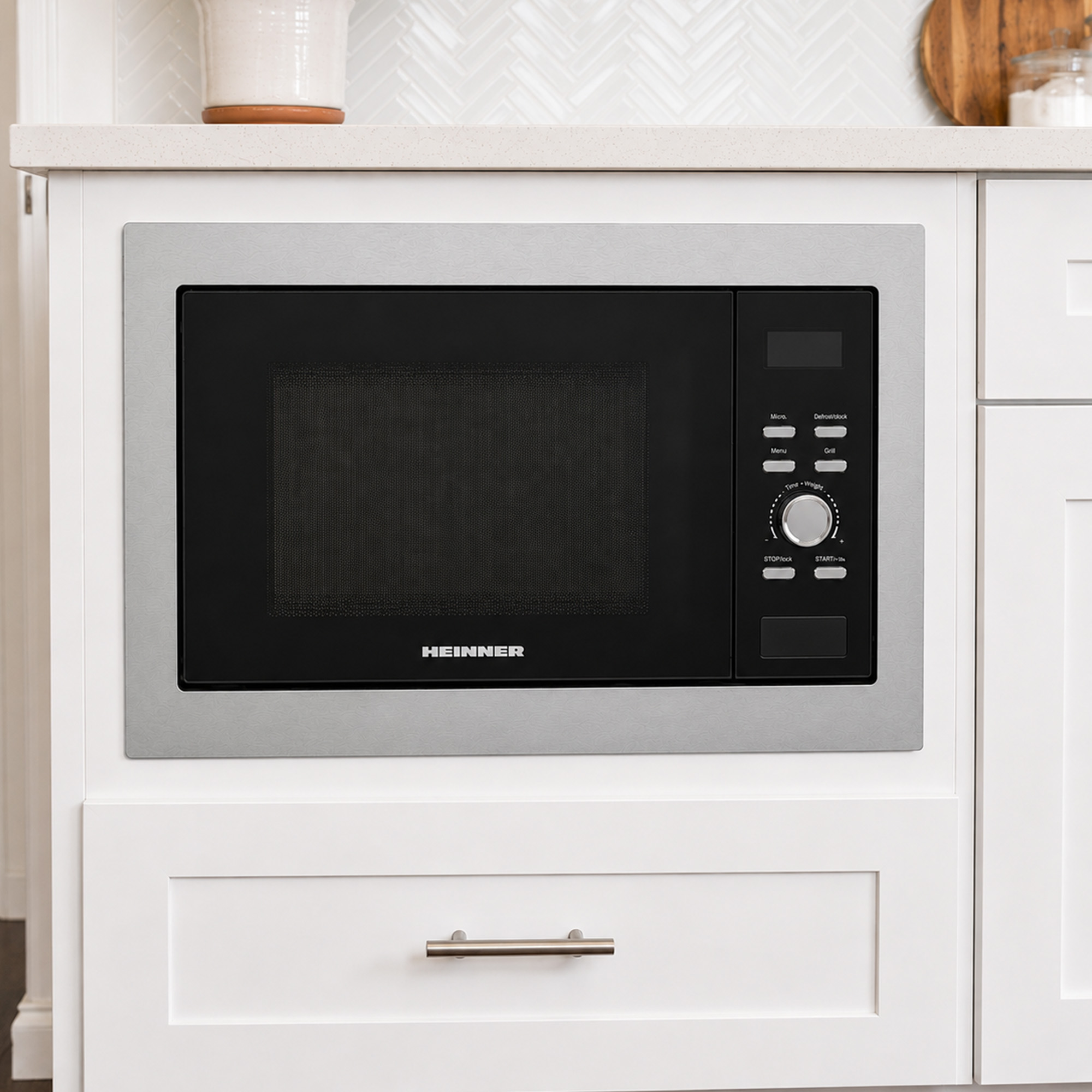 A built-in Heinner microwave with a silver frame, black door, and digital panel, set in a white kitchen cabinet.