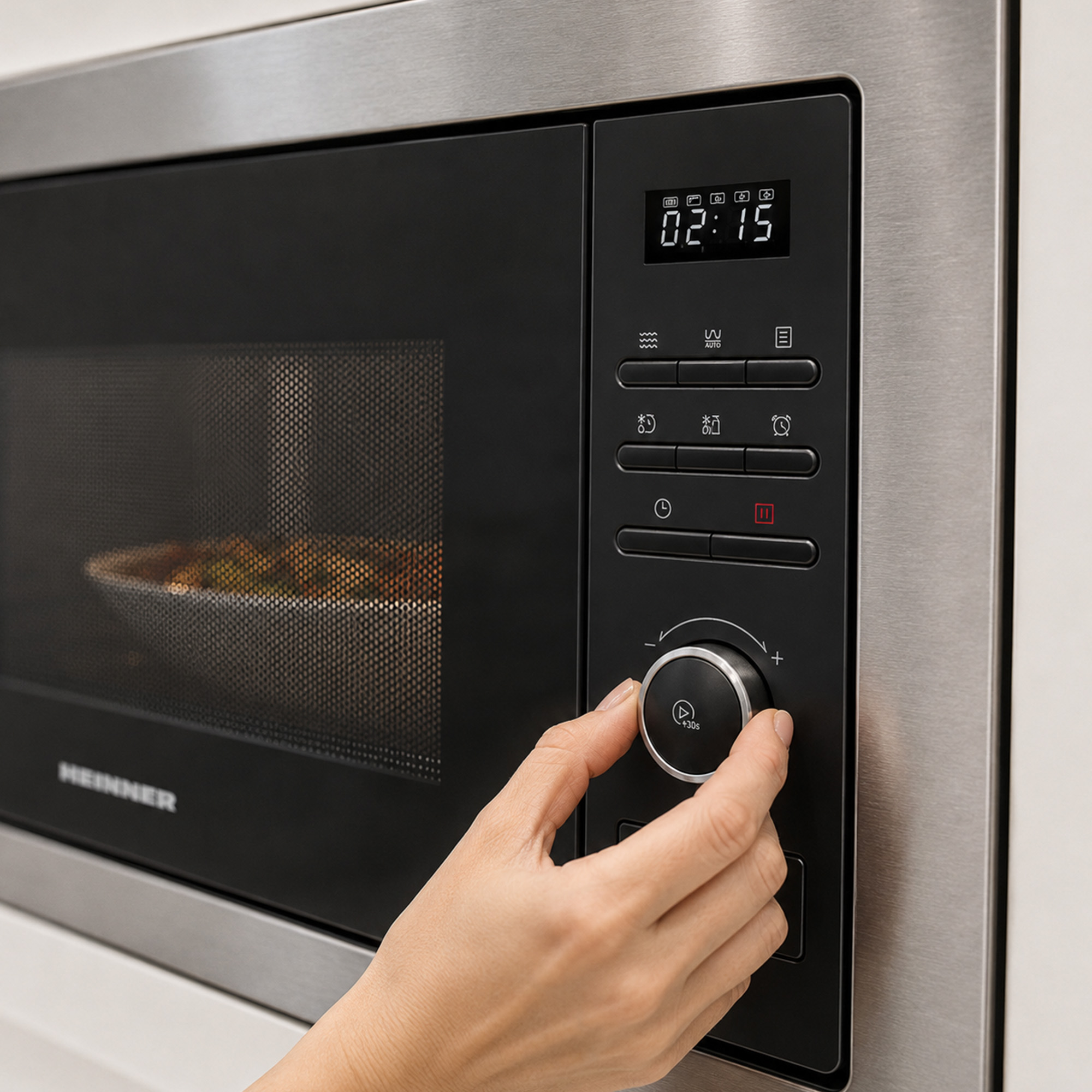 A hand turns the round control knob of a silver microwave with a digital display.