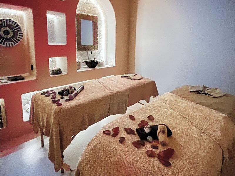 Una sala de spa con dos camillas de masaje, decoradas con pétalos y toallas, ante una pared naranja.
