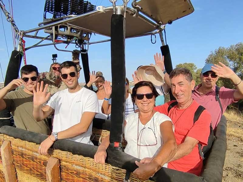 Un grupo de personas felices saluda desde el interior de una cesta de globo aerostático.