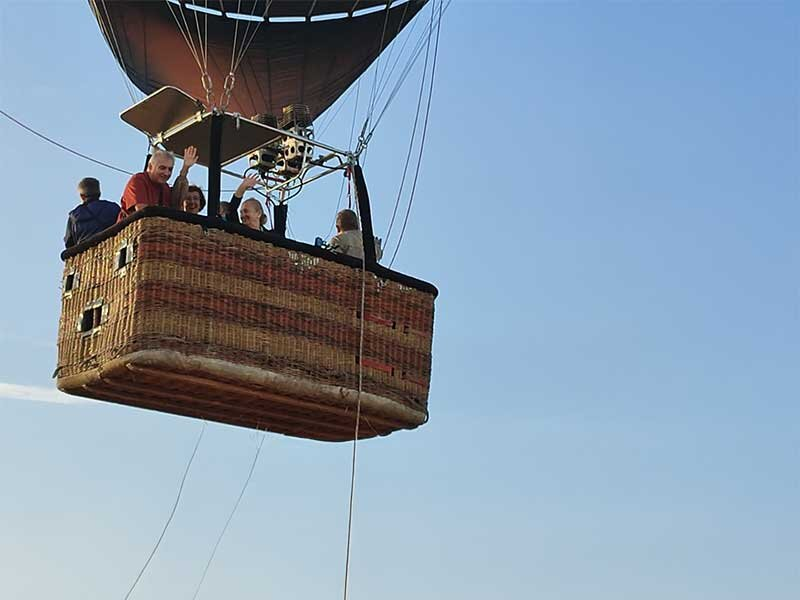 Personas saludando desde la cesta de un globo aerostático en el cielo.
