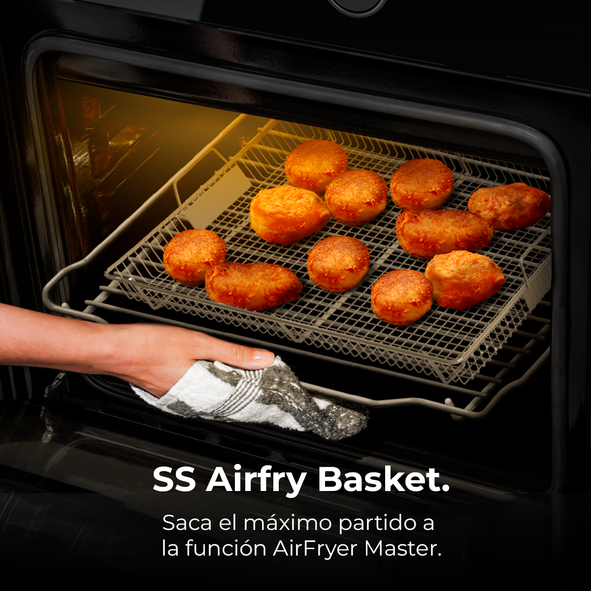 Una mano usa un paño para sacar una cesta de freidora de aire con comida dorada de un horno.