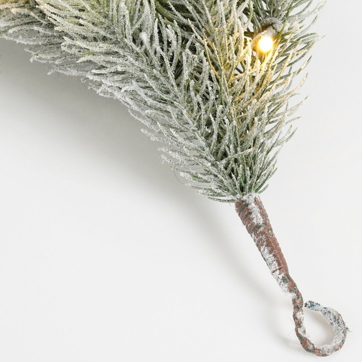 Ein frostiger künstlicher Tannenzweig mit befestigter Lichterkette auf weißem Hintergrund.