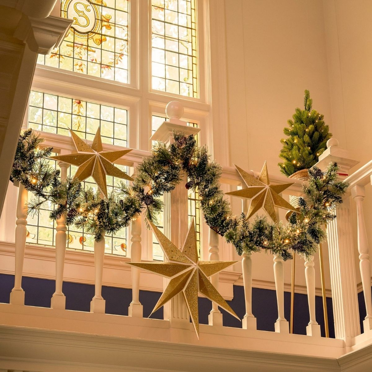 Weihnachtsgirlande mit goldenen Sternen und Lichtern auf weißem Treppengeländer.
