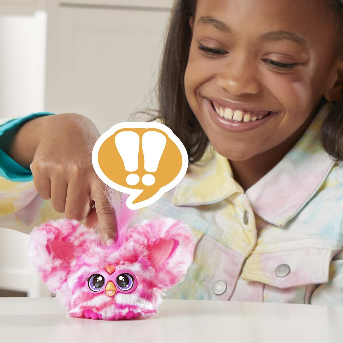 Una niña feliz tocando un juguete mullido rosa y blanco con ojos grandes en una mesa.