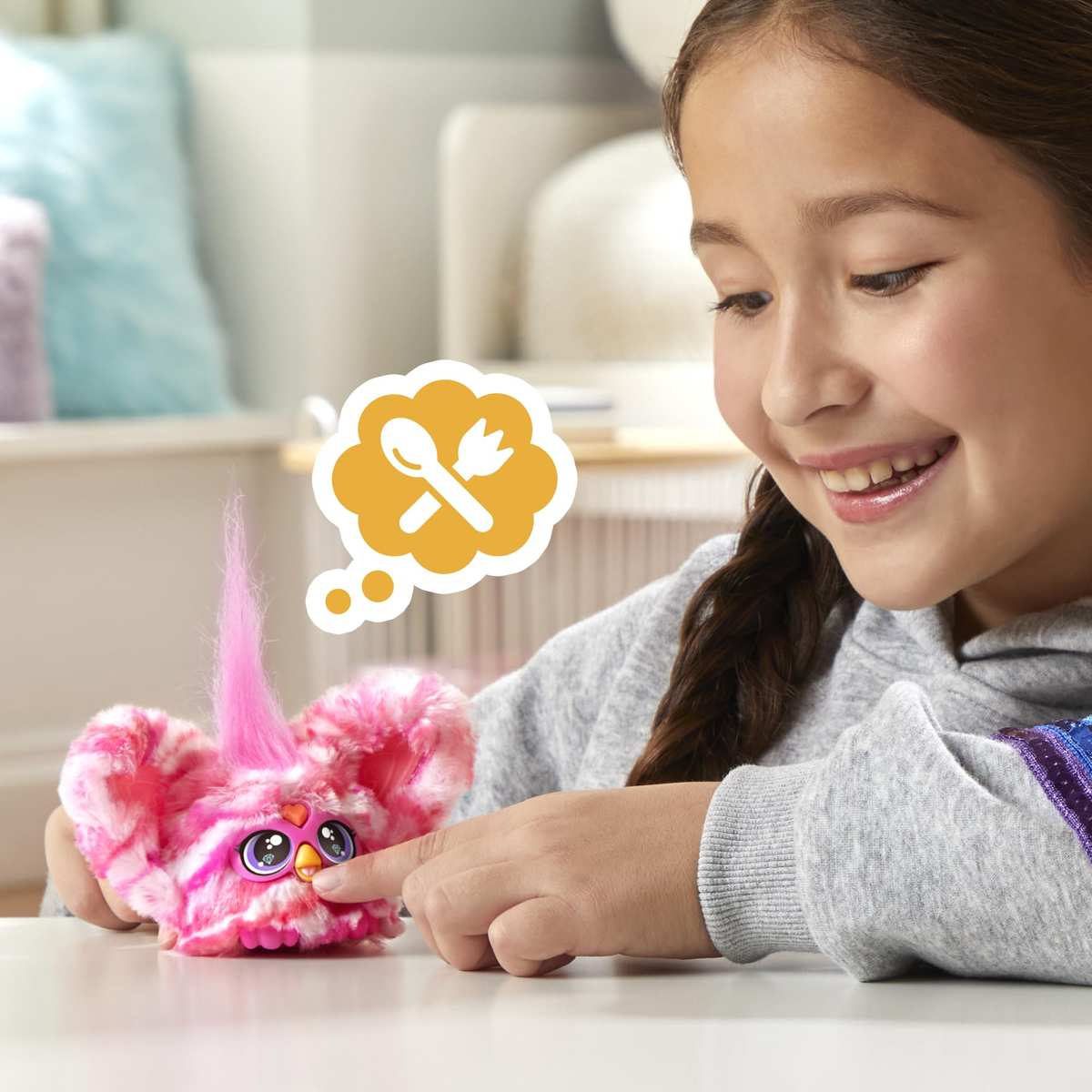 Una niña sonriente alimenta un juguete peludo rosado de Furby, con un icono de comida flotando.