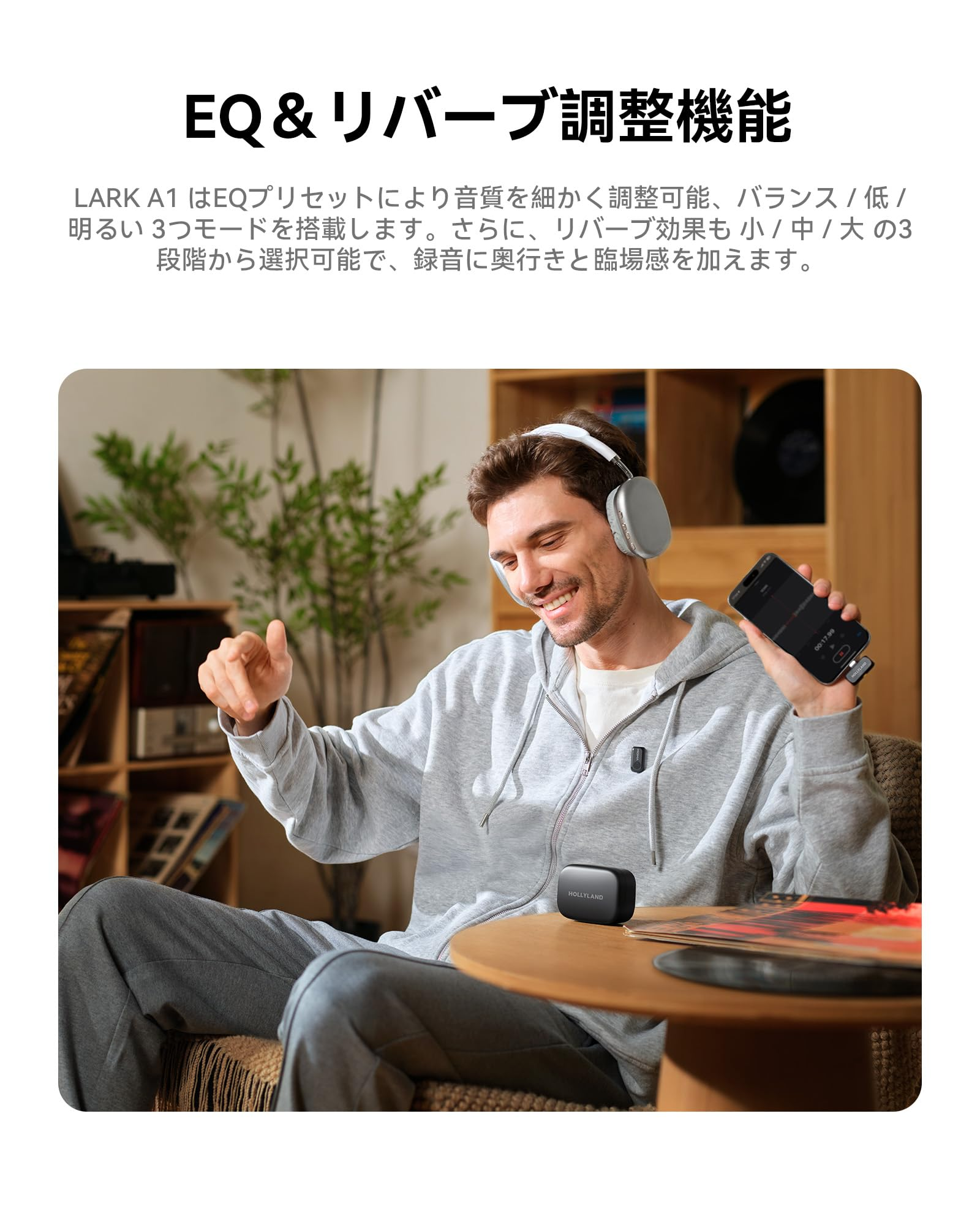 Ein Mann mit Kopfhörern lächelt, hält ein Smartphone und sitzt entspannt in einem Zimmer mit Holztönen.