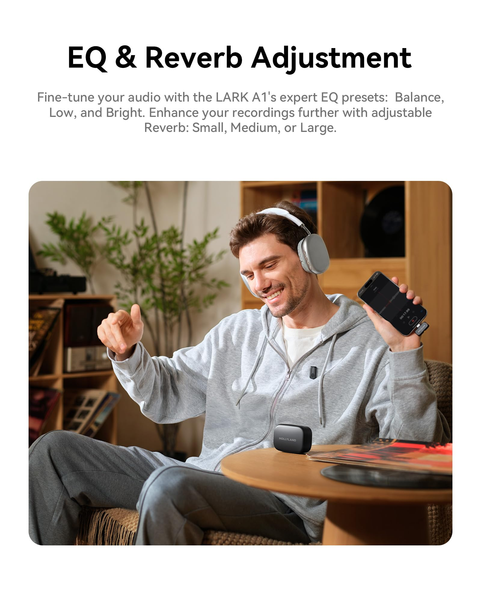 Ein junger Mann mit Kopfhörern lächelt, während er in einem Wohnzimmer eine Audioaufnahme mit dem Smartphone steuert.