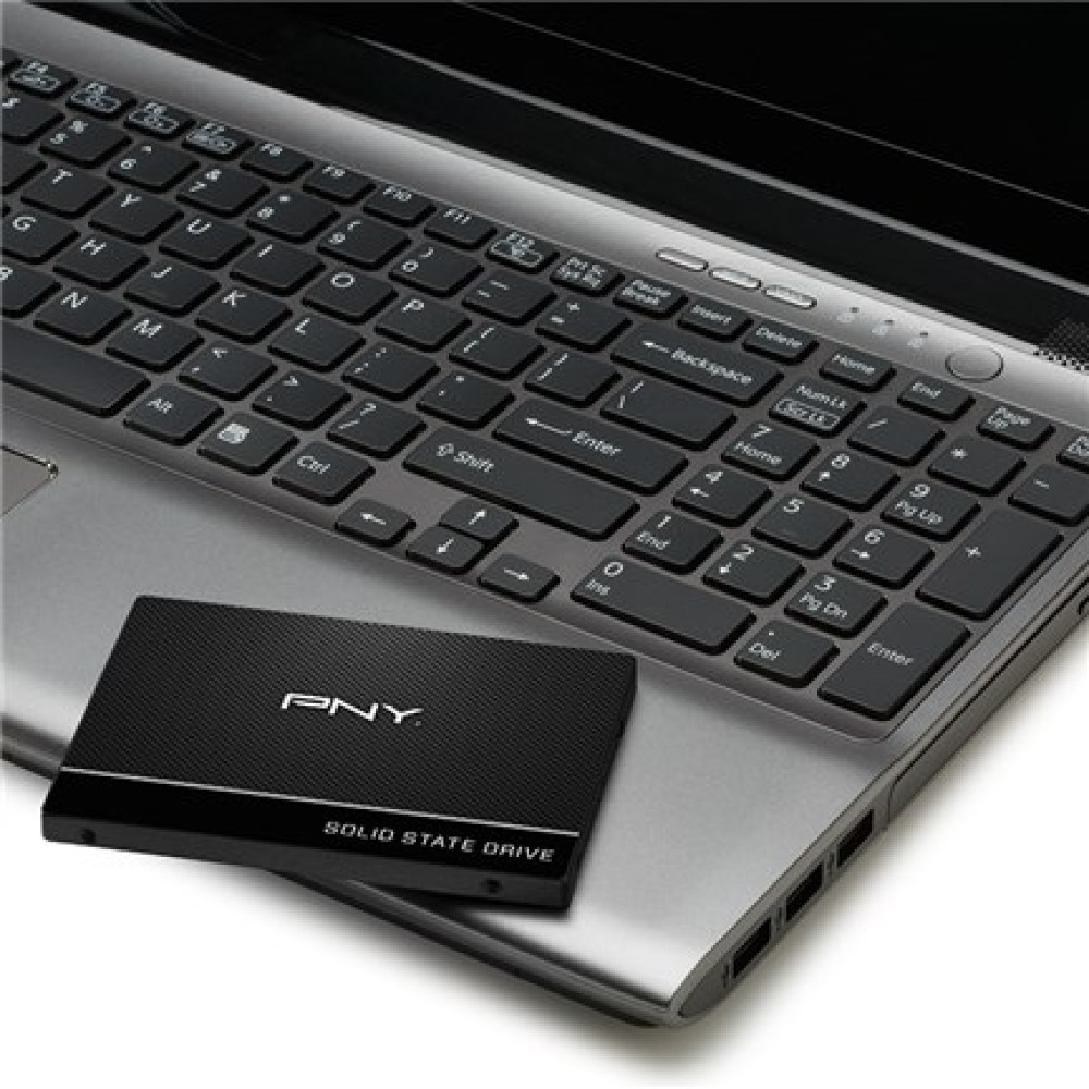 A black PNY solid state drive rests on the palm rest of a silver laptop.