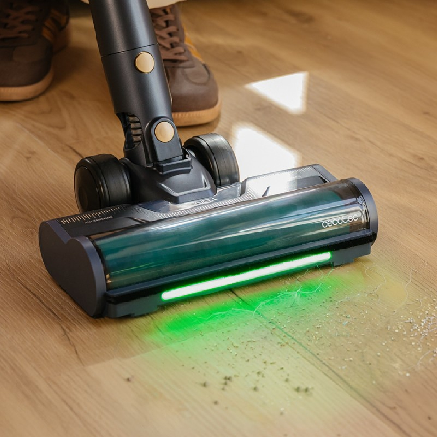Una aspiradora gris con luz verde ilumina la suciedad en un suelo de madera.