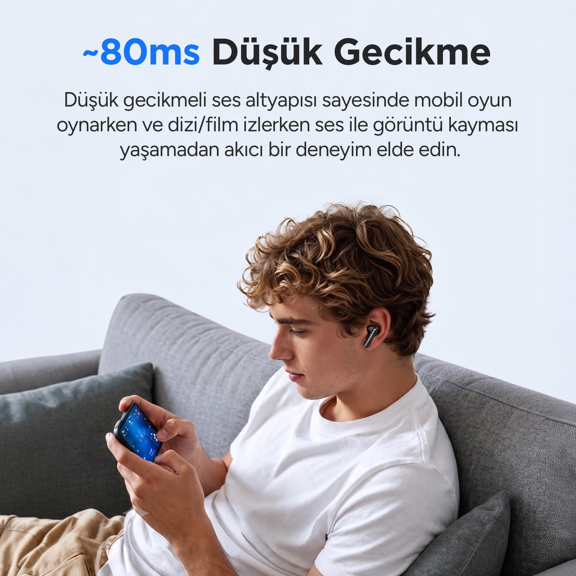 Kulaklıklı genç bir adam kanepede oturmuş mobil oyun oynuyor.