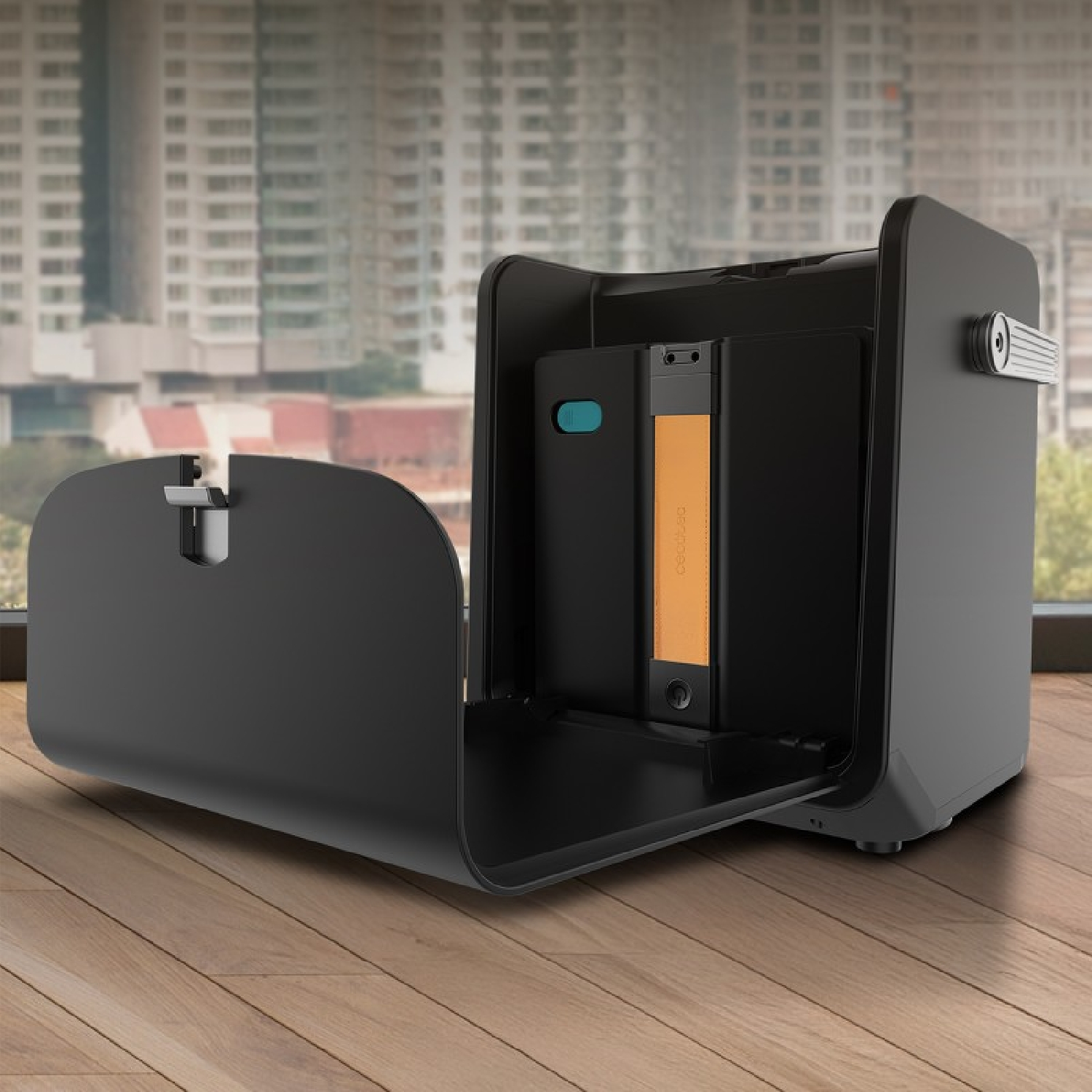 Una custodia nera aperta con una batteria arancione all'interno si trova su un pavimento di legno davanti a una finestra.