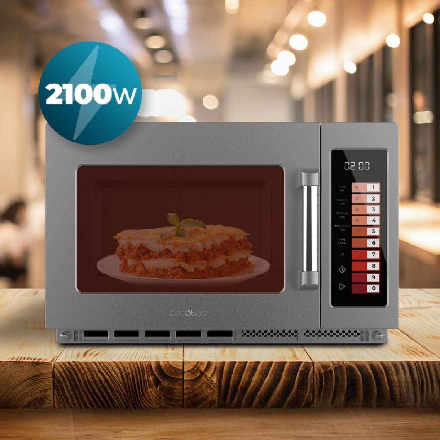 Un microondas gris en una mesa de madera con lasaña dentro y una pegatina azul que muestra 2100W.