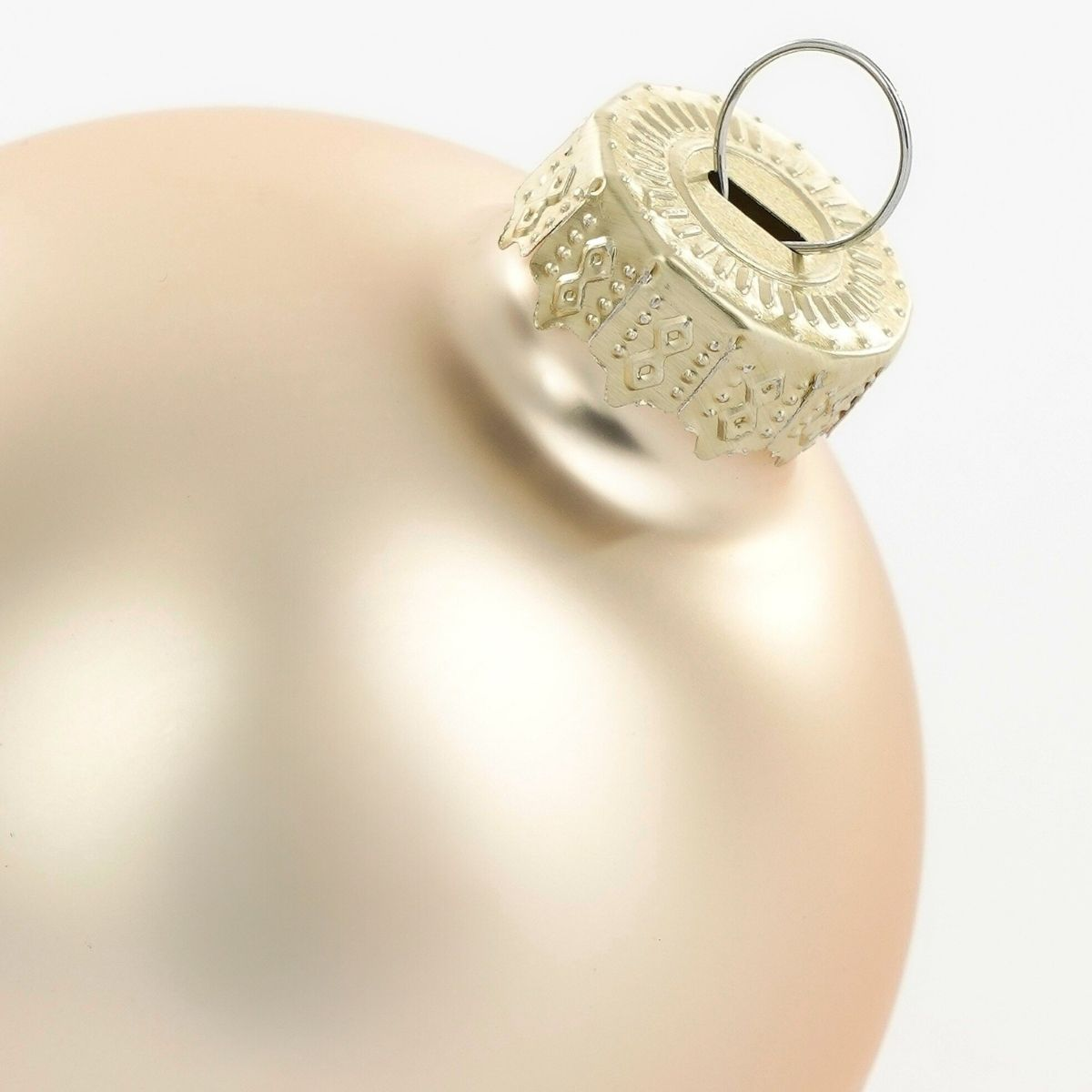 A matte champagne-colored Christmas ornament ball with an ornate gold cap and hanging ring.