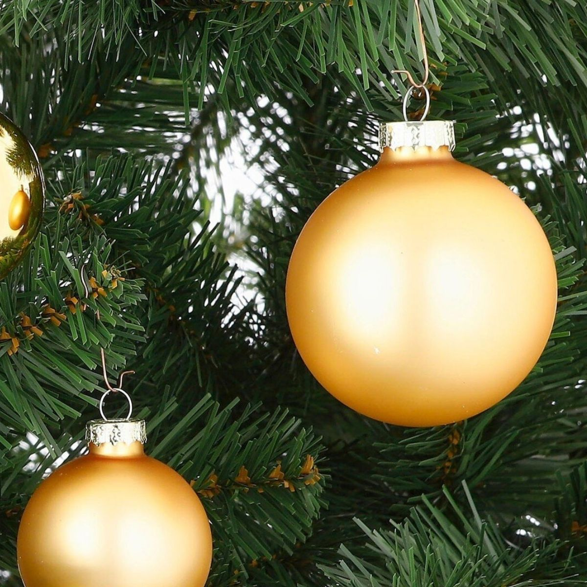 Shiny gold Christmas baubles hang from the branches of a green artificial Christmas tree.