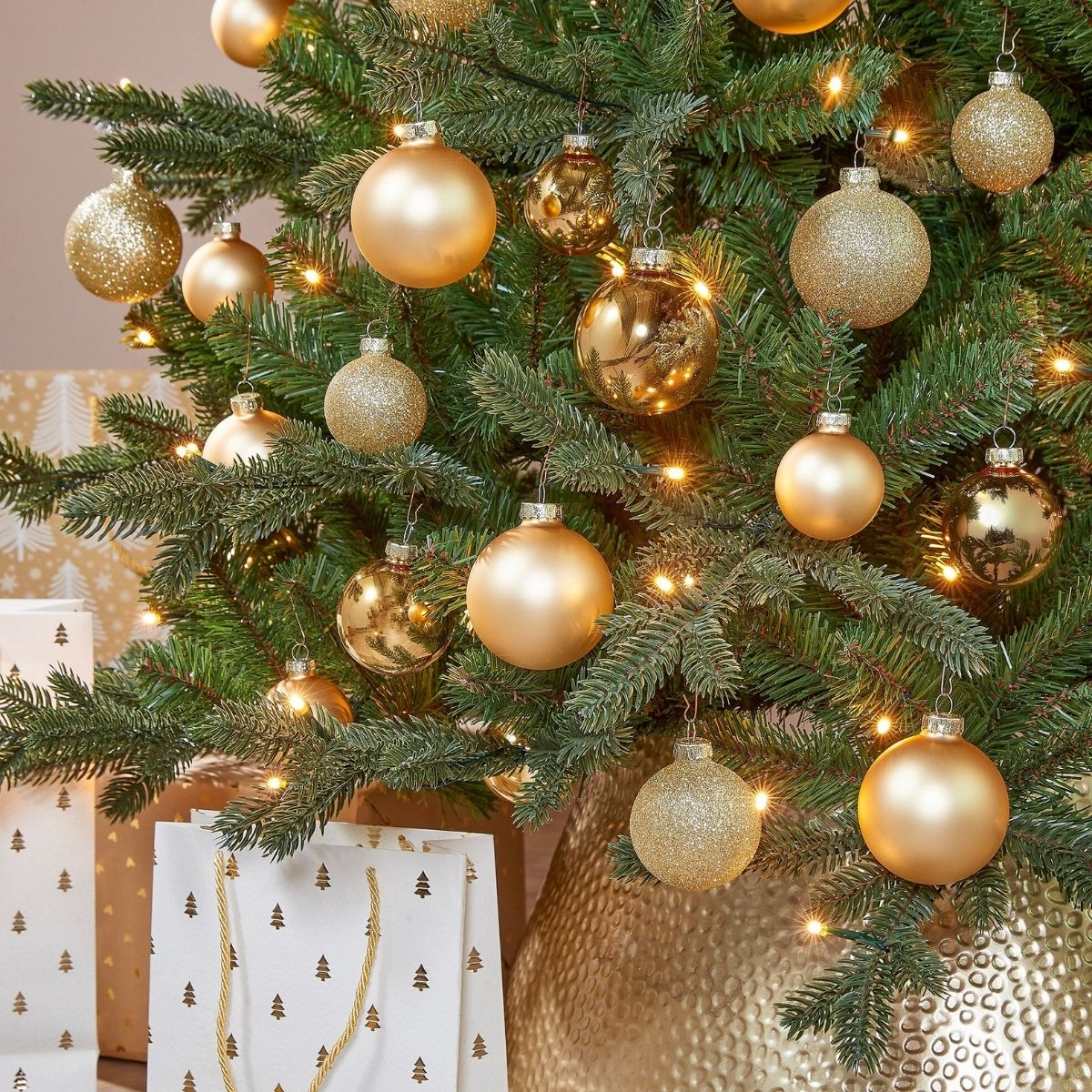 A Christmas tree decorated with gold baubles and lights, with gift bags on the floor.
