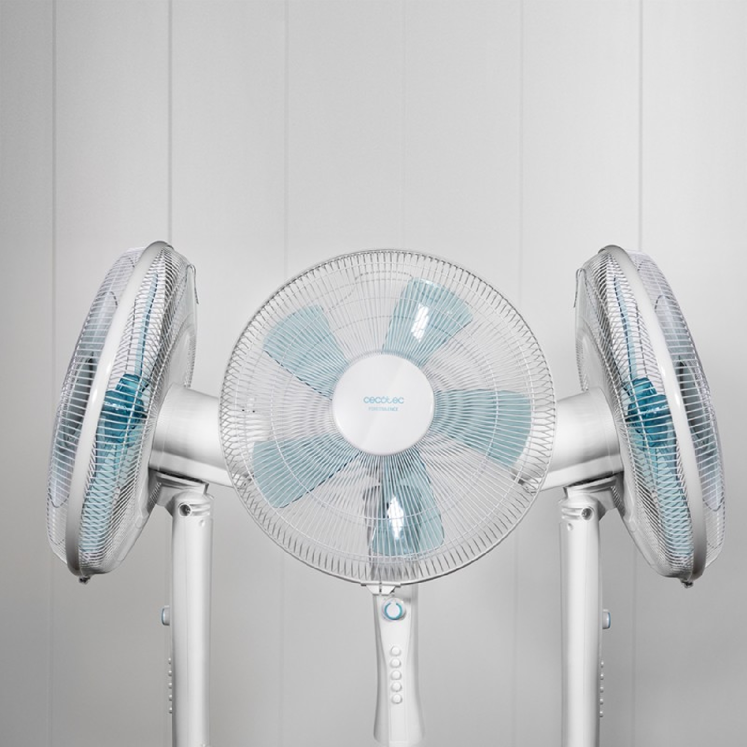 Tres ventiladores de pie blancos con aspas azules están uno al lado del otro contra una pared lisa.