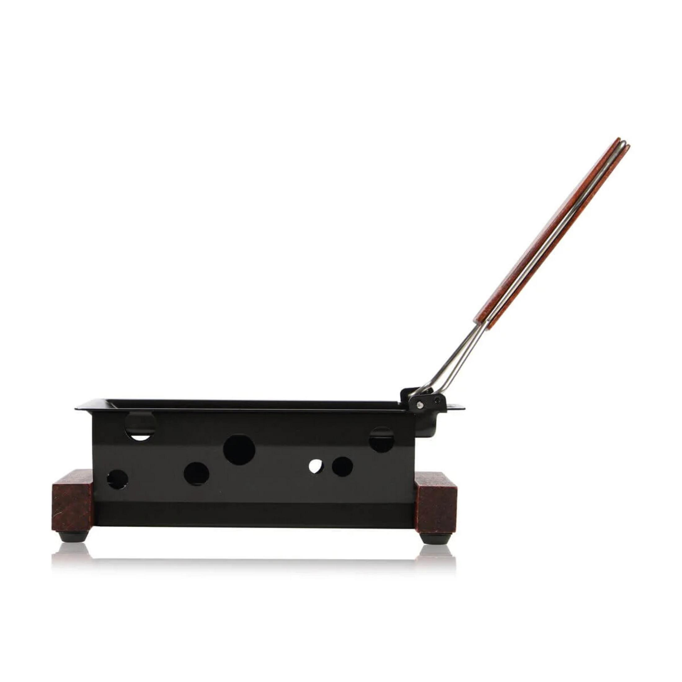 Ein schwarzer Raclette-Ofen mit perforierten Seiten und einem Holzgriff, der auf einem weißen Hintergrund steht.